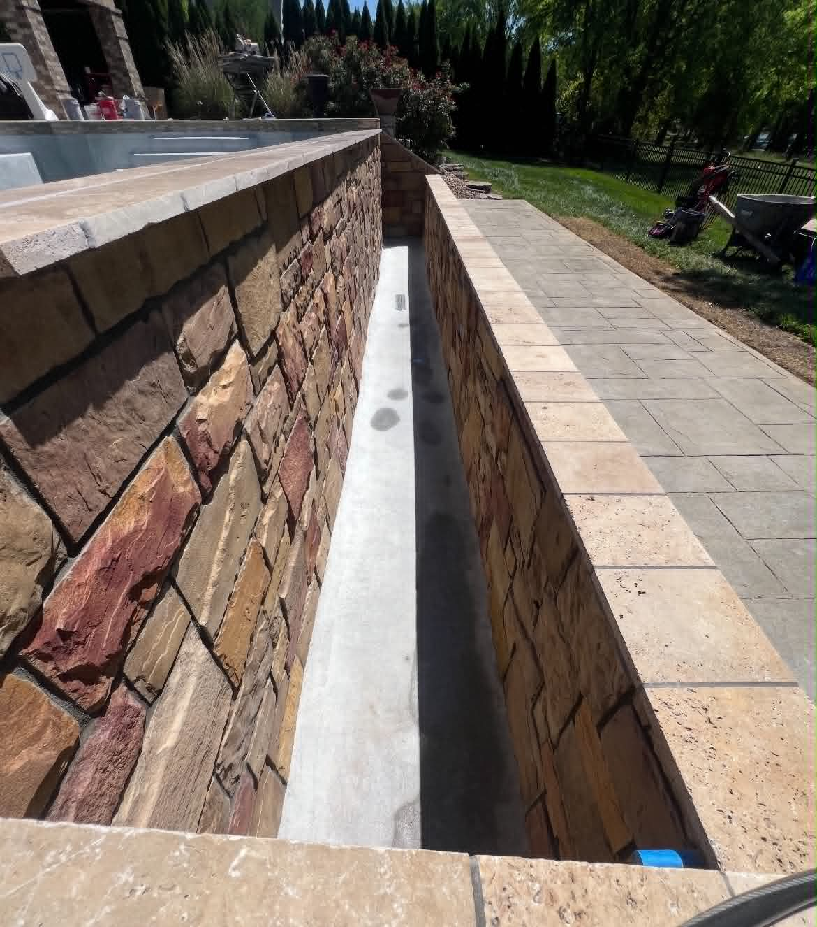 Multi-tone natural stone wall detail beside a stamped concrete patio and pool