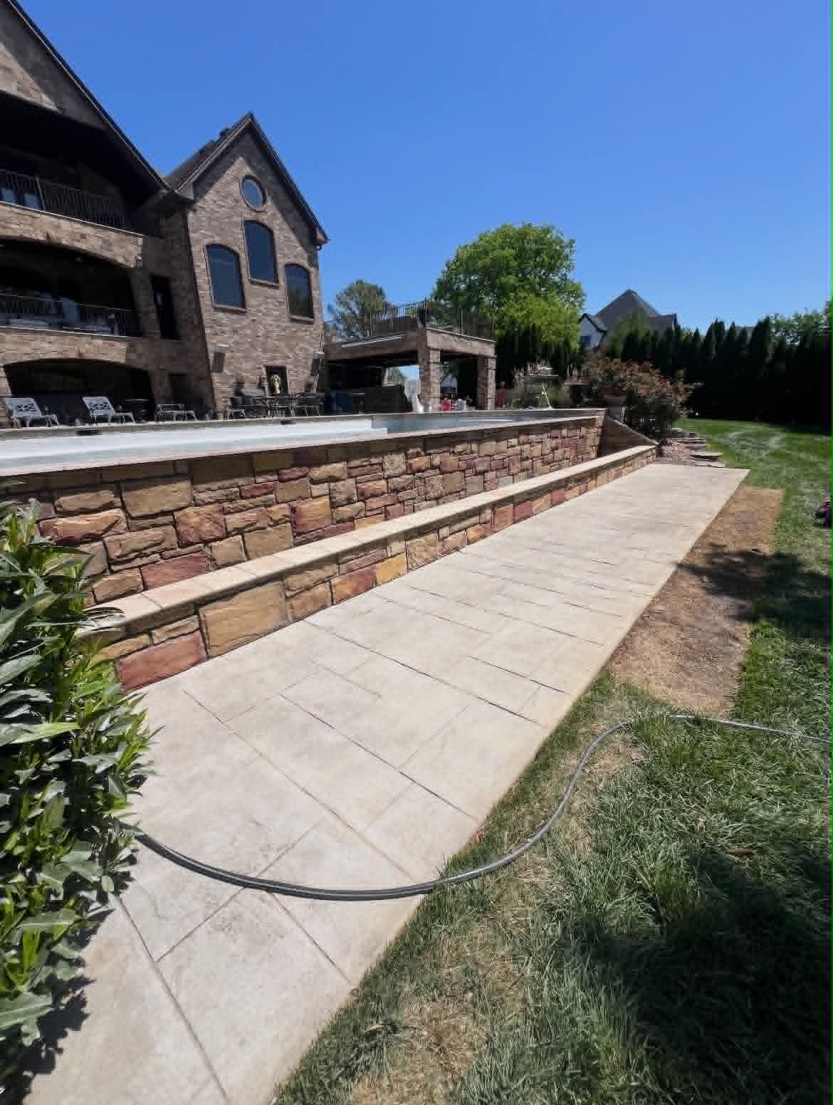 Stamped concrete walkway alongside a natural stone retaining wall by an infinity pool