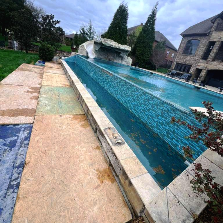 Finished travertine pool deck with mosaic-tile infinity pool and rock waterfall