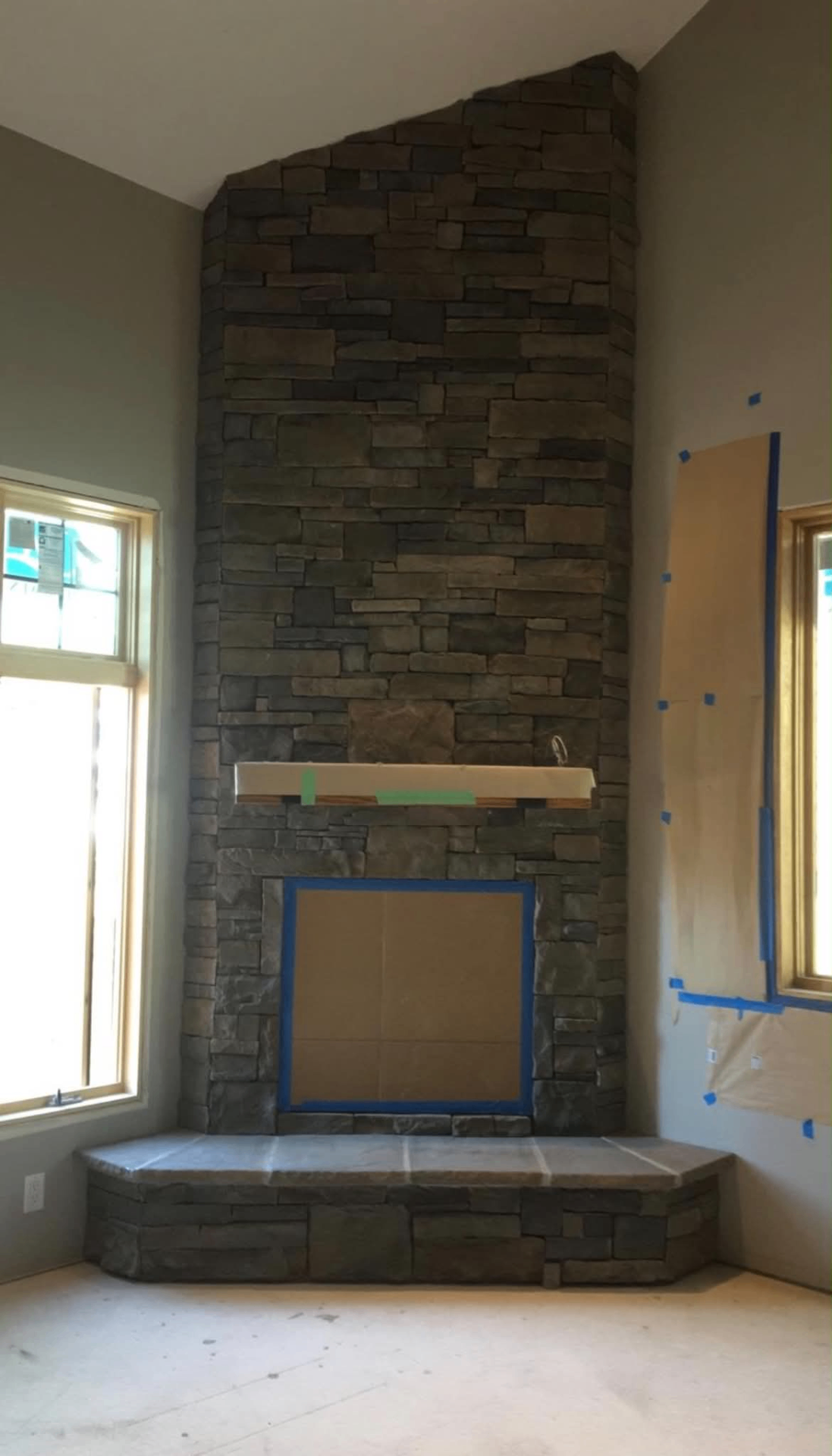 Floor-to-ceiling stacked stone fireplace with hearth and mantel in progress
